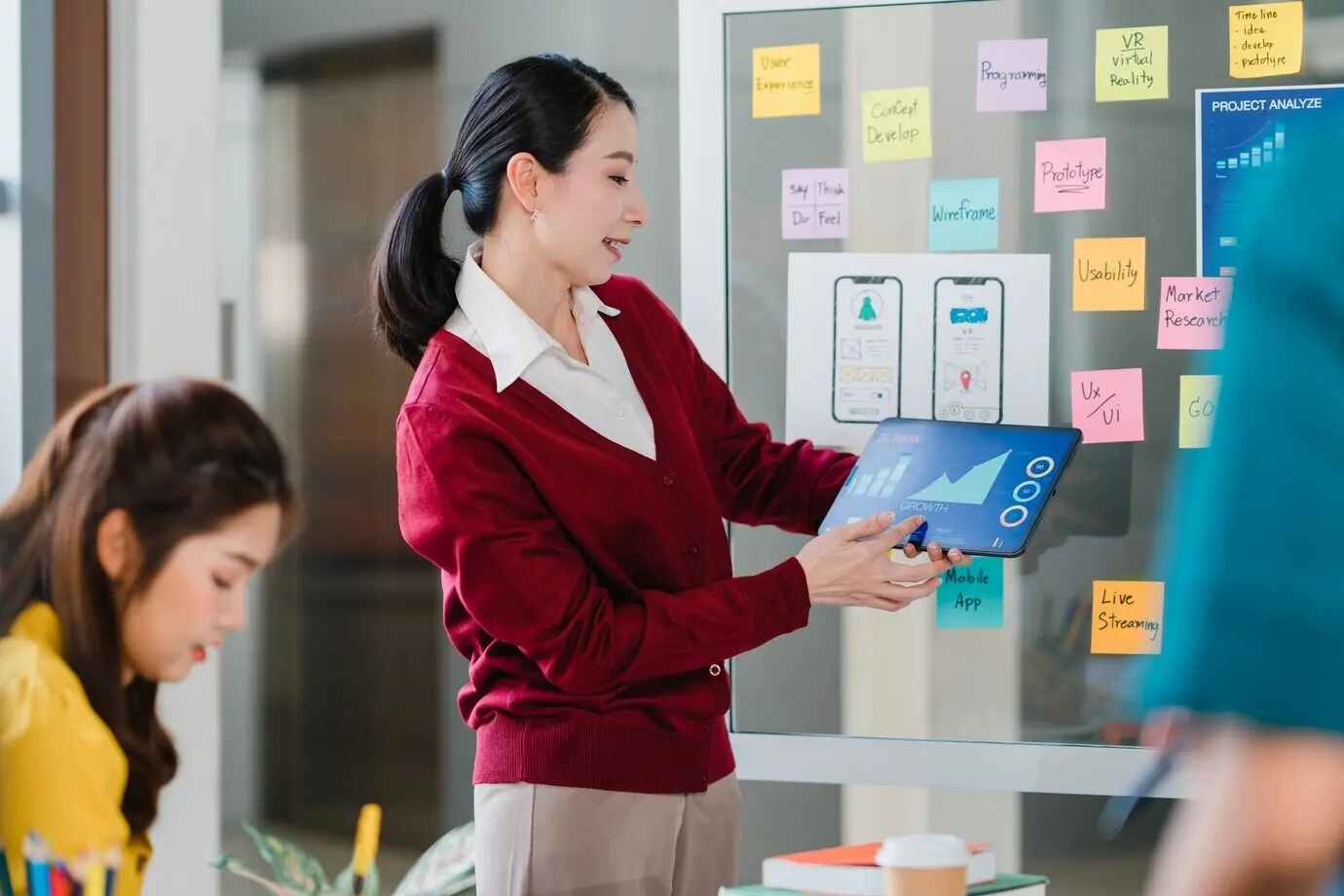 Группа молодых креативных людей из Азии на встрече проводит мозговой штурм и бизнес-презентацию идей для проекта по проектированию программного обеспечения мобильного приложения; коллеги в современном офисе, концепция командной работы коллег.